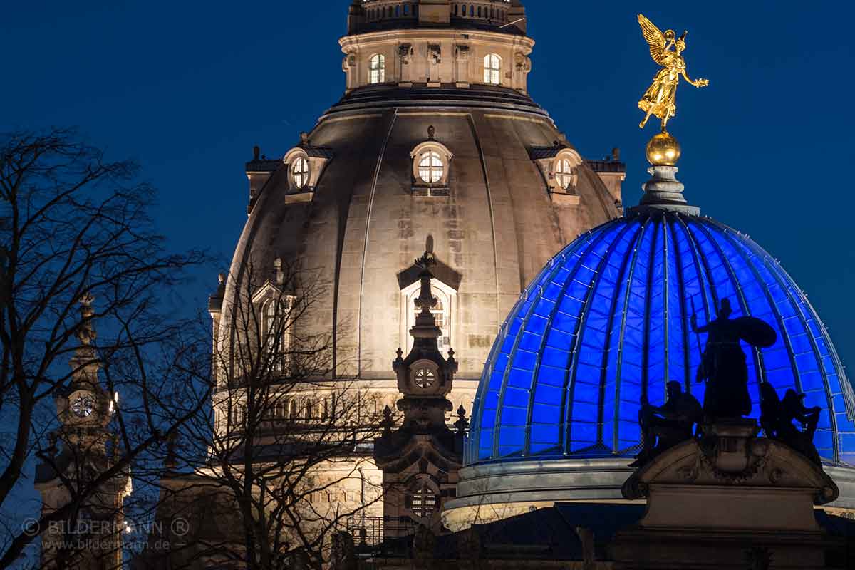 Blau angestrahlte Glaskuppel des Sächsischen Kunstvereins mit Fama-Figur „Trompetenengel“ vor der Sandsteinkuppel der Dresdner Frauenkirche